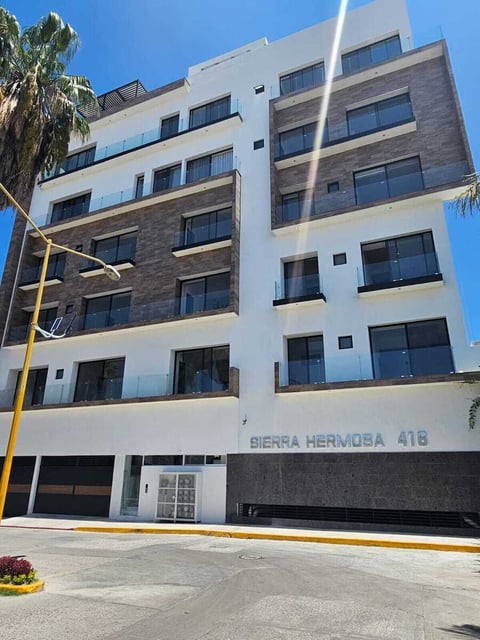 Modern multi-story apartment building with white and stone facade, numbered Tierra Hermosa 418, featuring large windows and ground-level parking